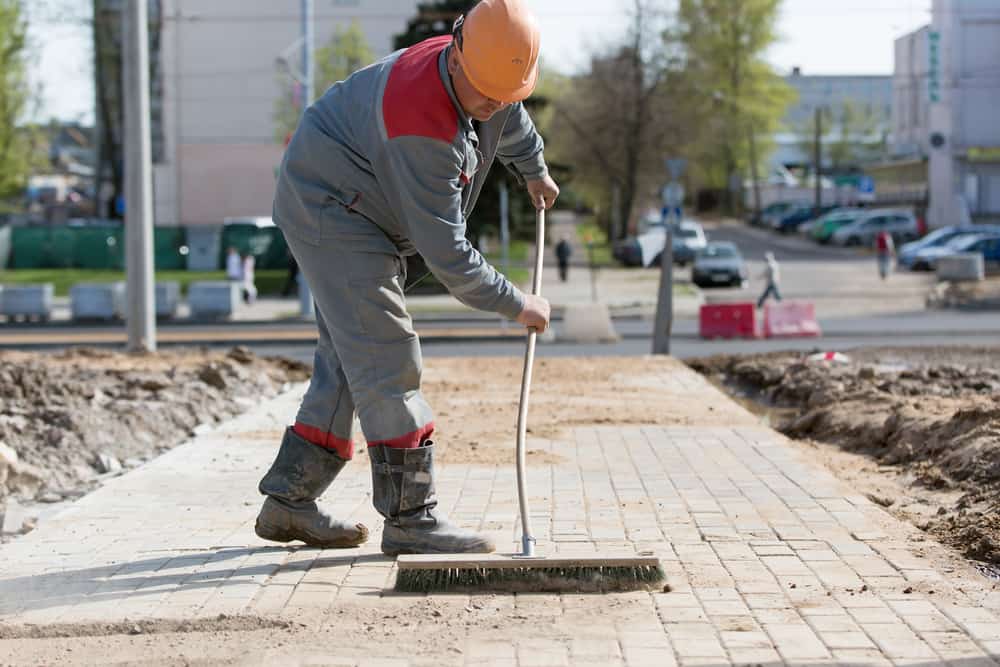 Construction Worker Grouting Dry Sand With Brush Into Paver Bricks